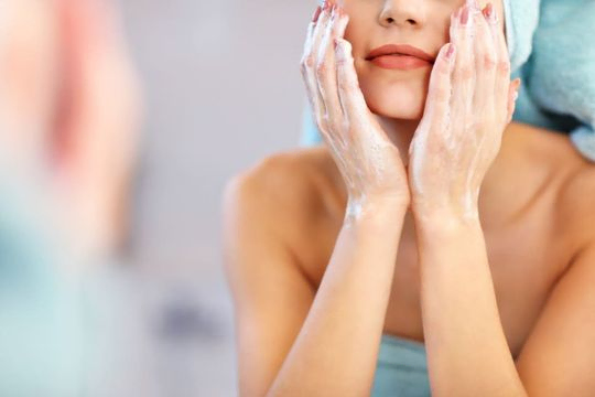 mujer limpiándose la cara frente al espejo